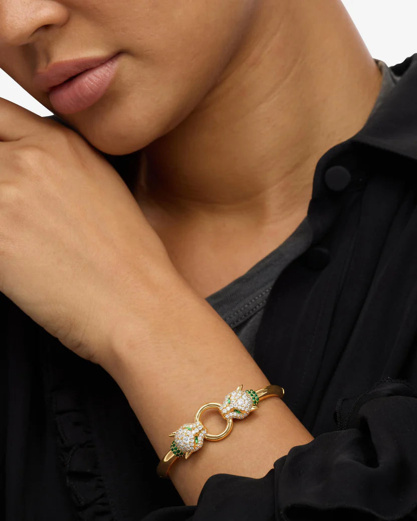 Close-up of a person wearing a gold bracelet with green gemstones on a black background