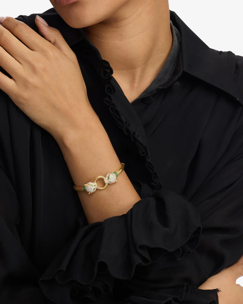 Close-up of a person wearing a gold bracelet with green gemstones on a black outfit.