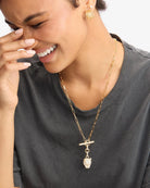 Woman wearing a gold necklace with a pendant, smiling.