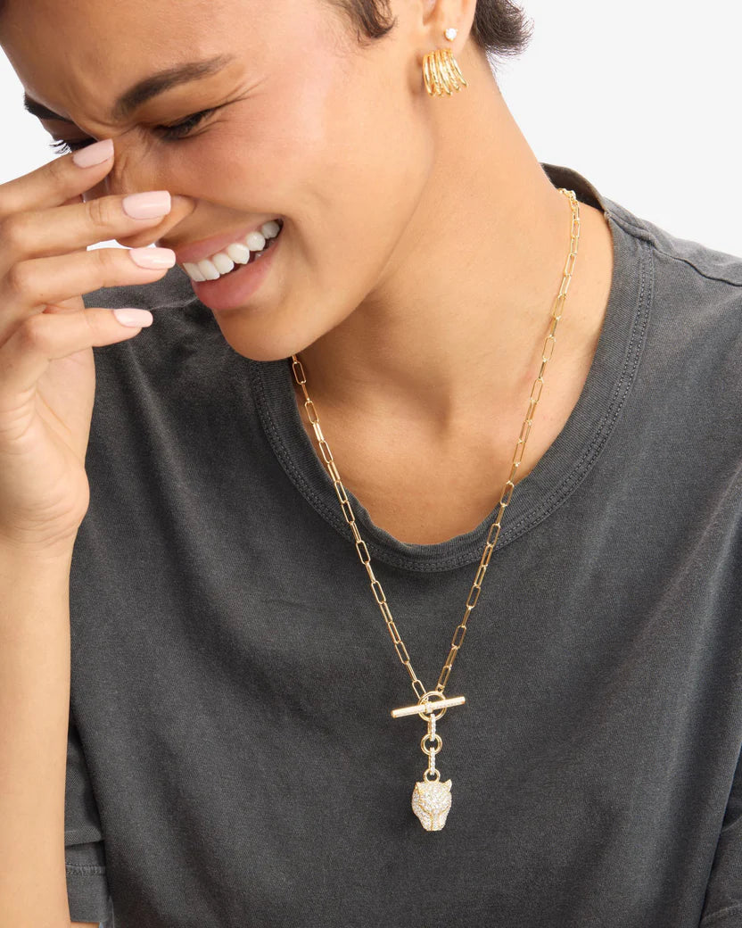 Woman wearing a gold necklace with a pendant, smiling.