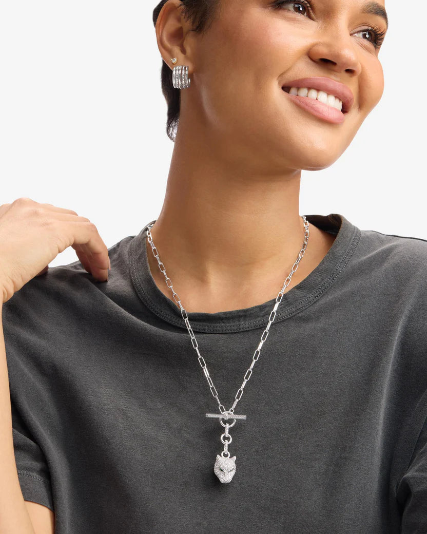 Woman wearing a silver necklace with a pendant on a plain background