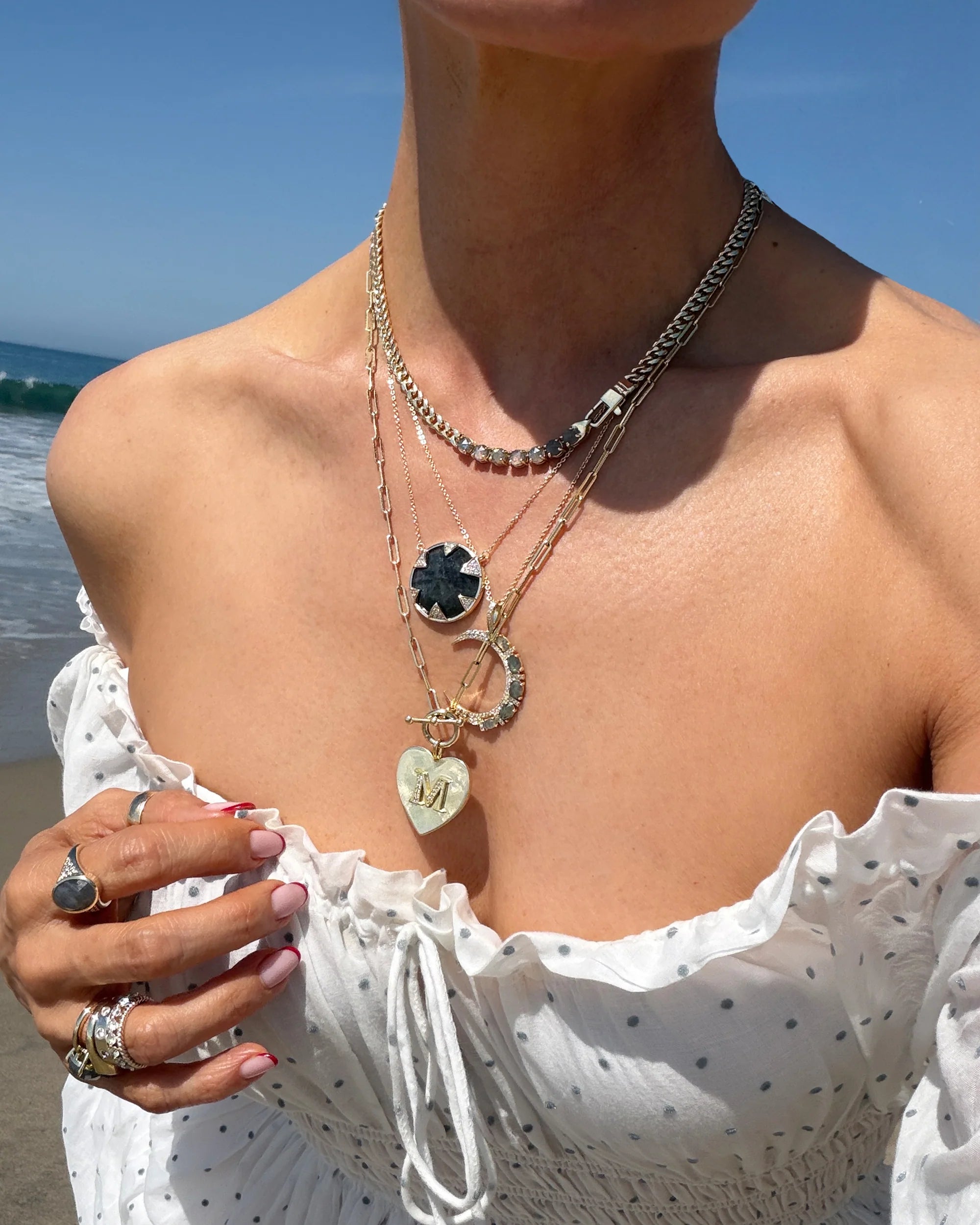 Person wearing layered necklaces with a beach background