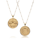 Two gold pendants on chains against a white background