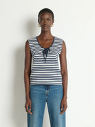 Woman wearing a striped tank top and jeans against a plain background