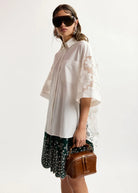 Woman wearing a white oversized shirt with lace sleeves, floral skirt, and sunglasses on a white background