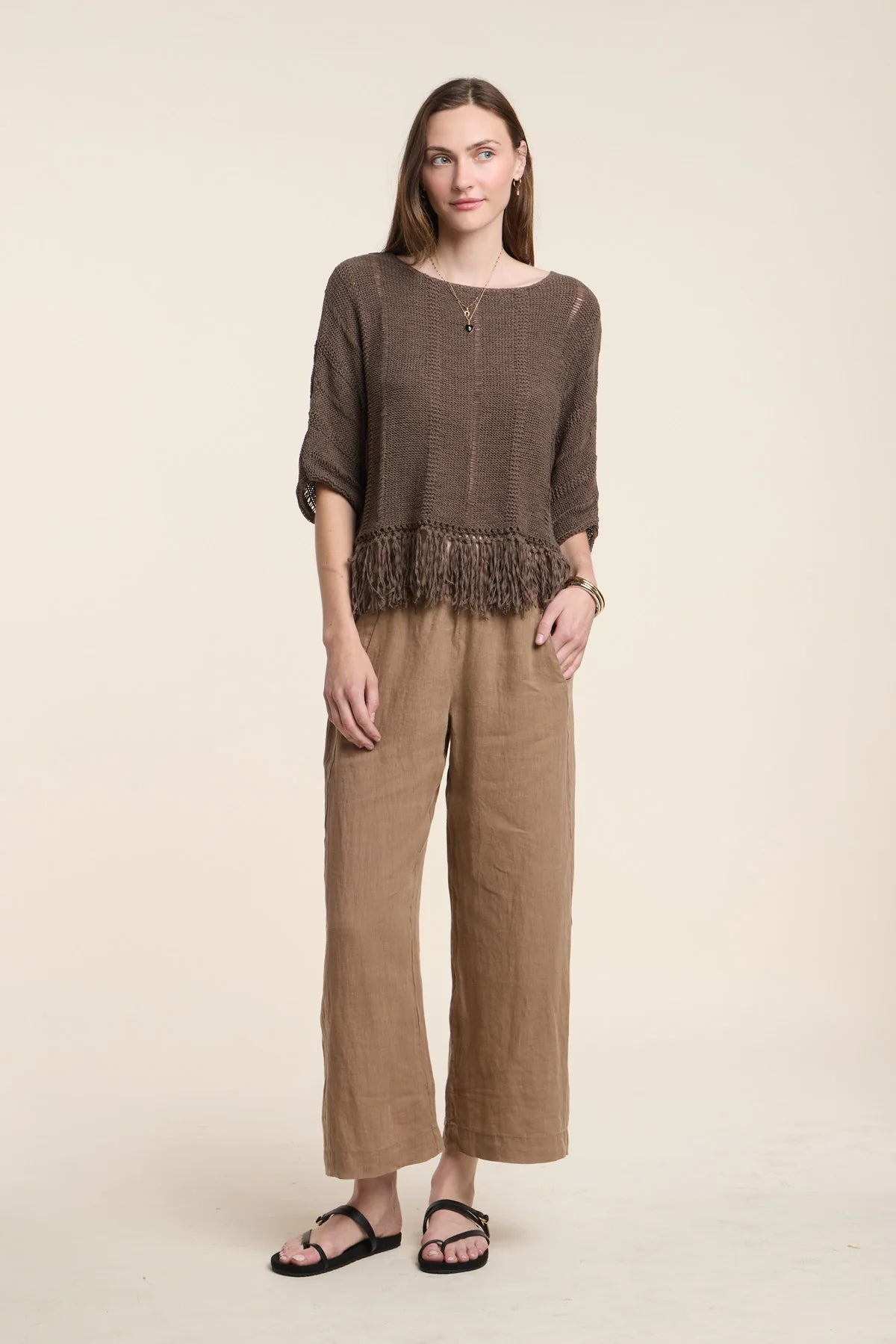 Woman wearing a brown fringe top and wide-leg pants on a beige background