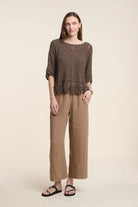 Woman wearing a brown fringe top and wide-leg pants on a beige background
