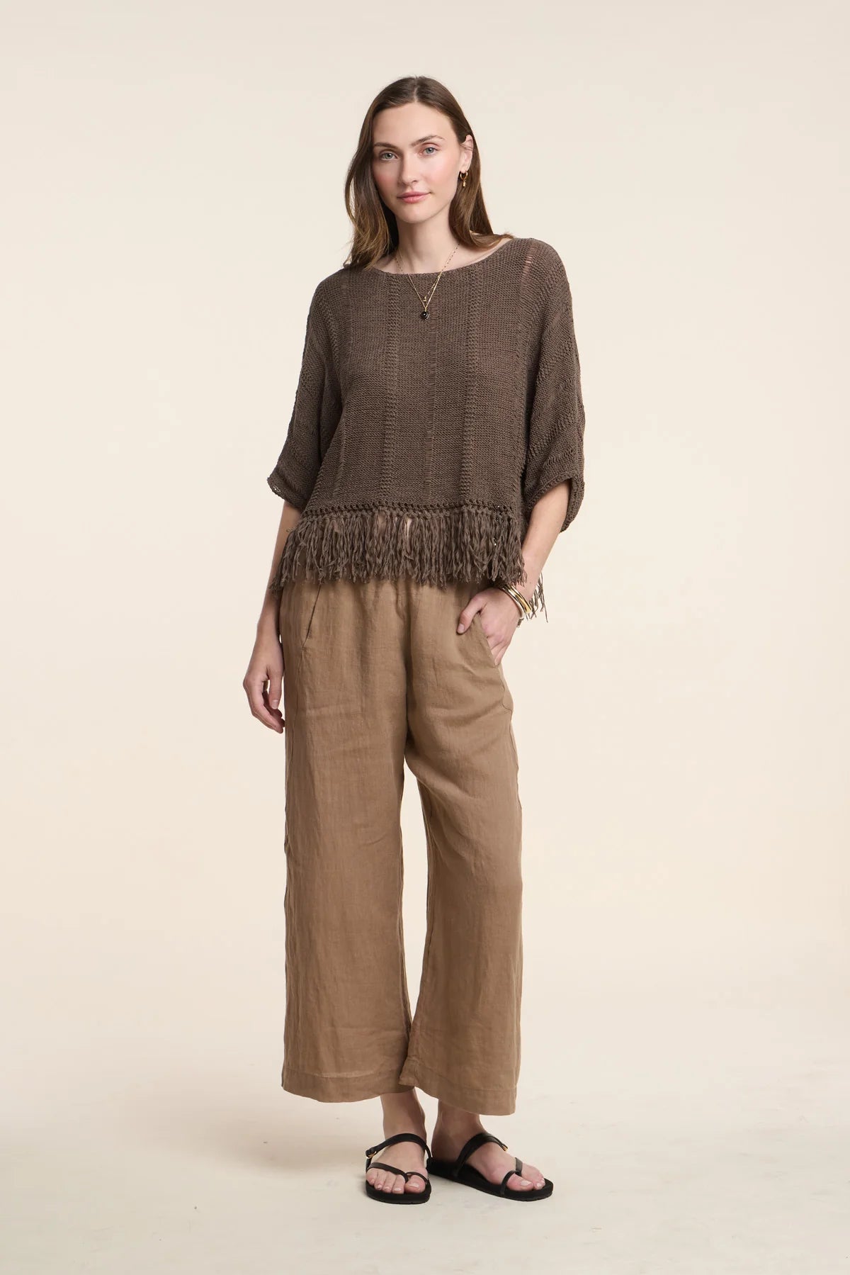 Woman wearing a brown fringe top and wide-leg pants on a beige background