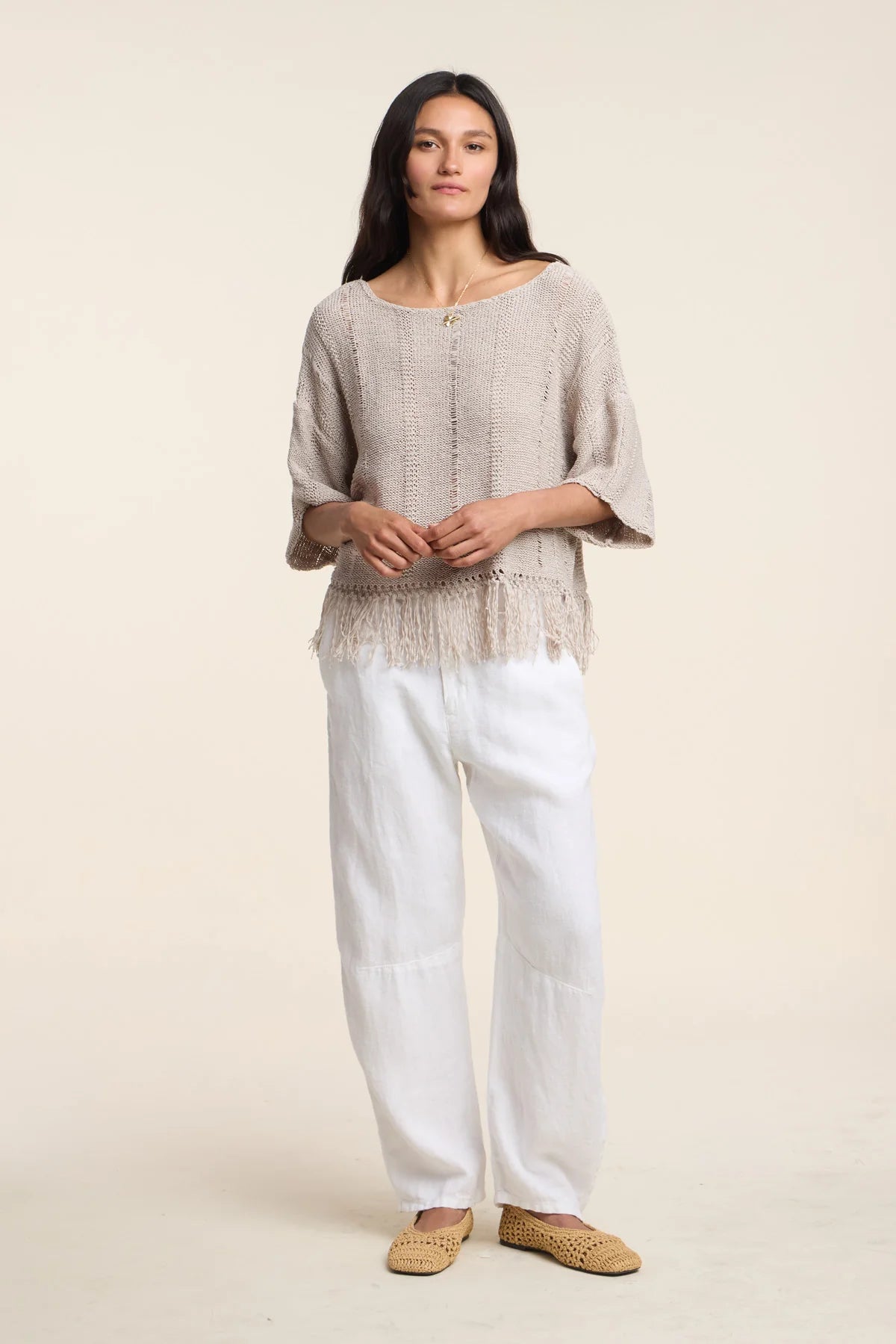 Woman wearing a beige top and white pants on a plain background