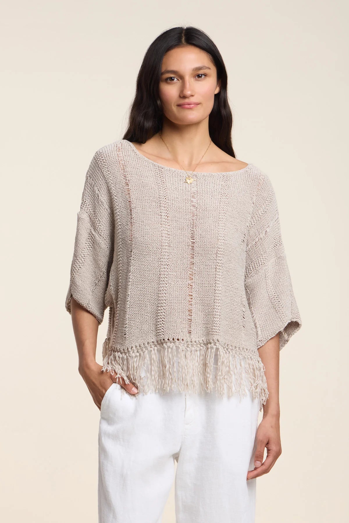 Woman wearing a beige knitted top and white pants on a beige background