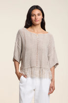 Woman wearing a beige knitted top and white pants on a beige background
