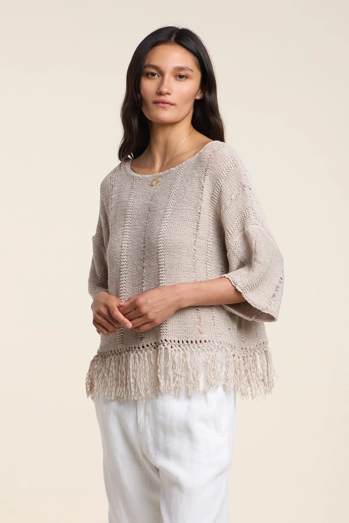 Woman wearing a beige knitted sweater with fringe on a beige background