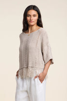 Woman wearing a beige knit poncho with fringe details on a beige background