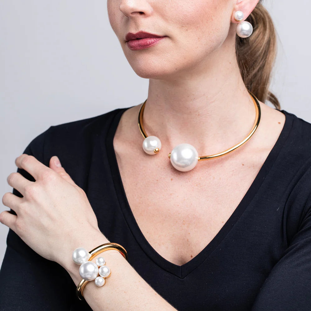 Woman wearing a gold necklace and pearl bracelet on a plain background