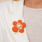 Orange flower brooch with pearl center on a white blazer