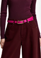A close-up of a person wearing a bright pink belt with a gold-tone buckle over a burgundy ribbed long-sleeve top and matching wide-leg trousers.