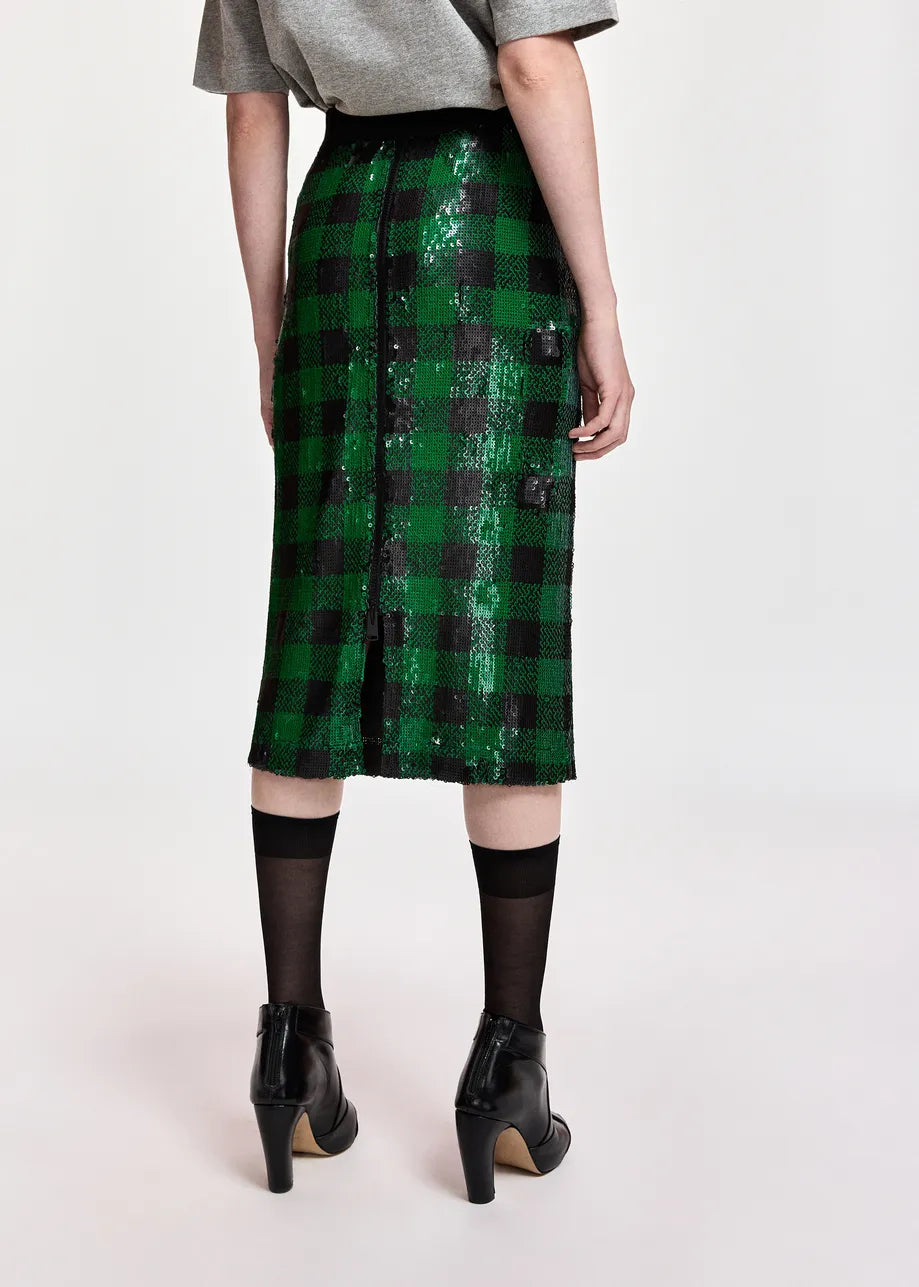 A model wearing a green and black sequined plaid midi skirt, styled with a gray t-shirt, black tights, and black ankle boots against a plain light background.