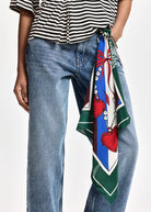 A close-up of a person wearing blue jeans and a black-and-white striped top, with a colorful patterned scarf tied around the waist over the jeans.