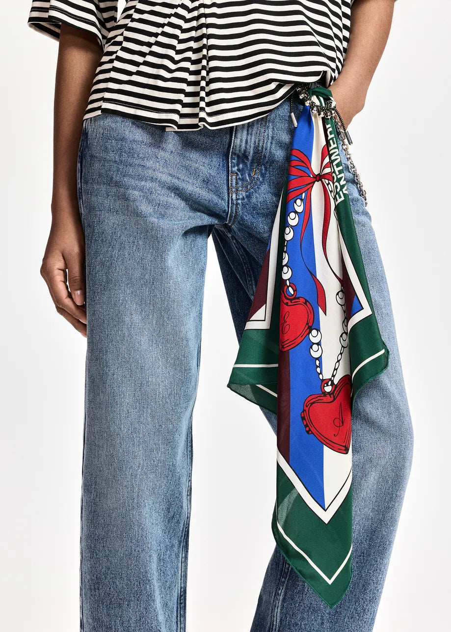 A close-up of a person wearing blue jeans and a black-and-white striped top, with a colorful patterned scarf tied around the waist over the jeans.