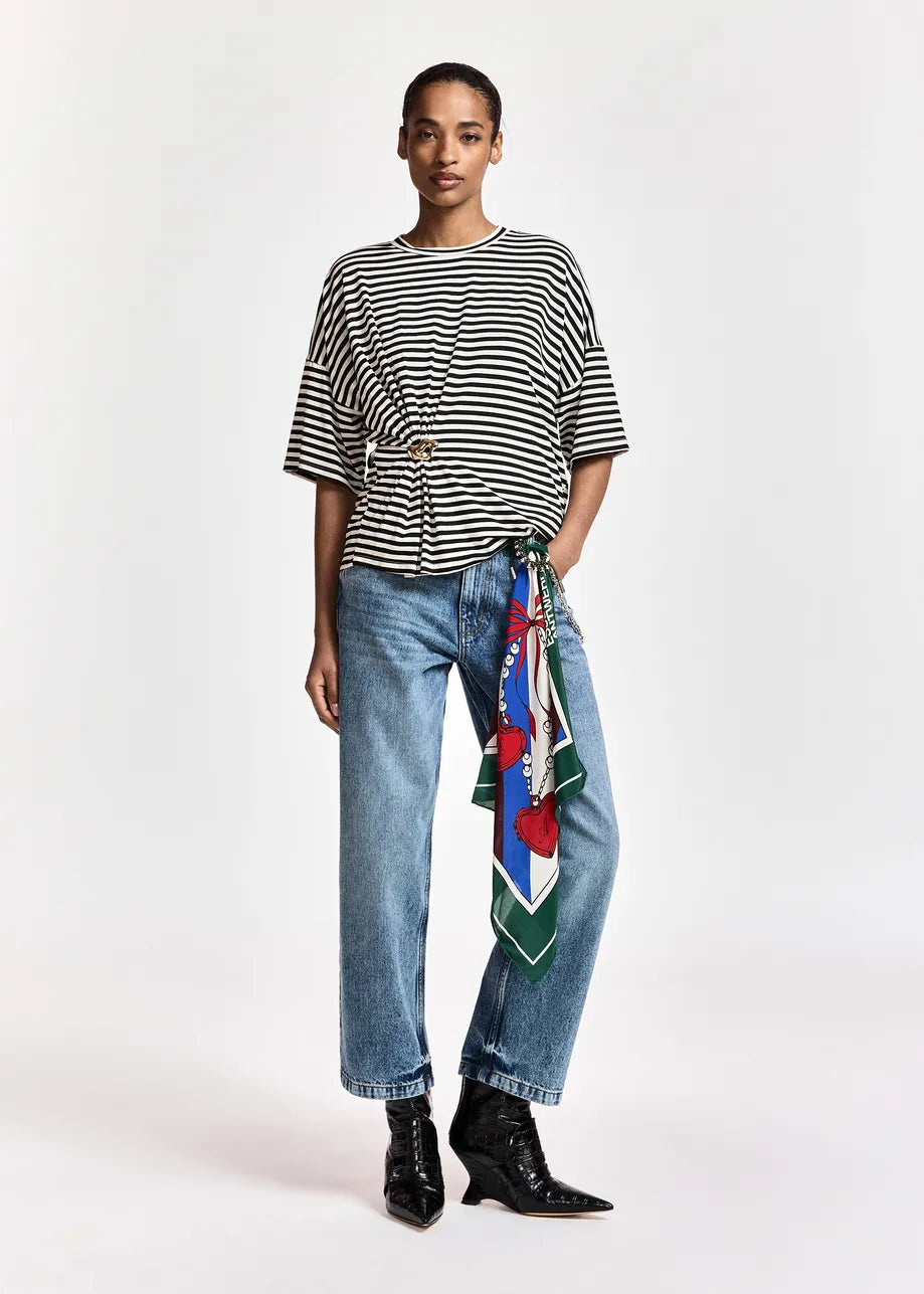 A close-up of a person wearing blue jeans and a black-and-white striped top, with a colorful patterned scarf tied around the waist over the jeans.