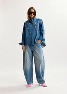 Person wearing a blue denim outfit with floral embellishments on a white background
