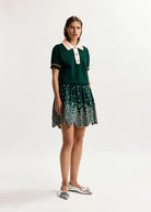 Woman wearing a green dress with a white collar and patterned skirt on a white background