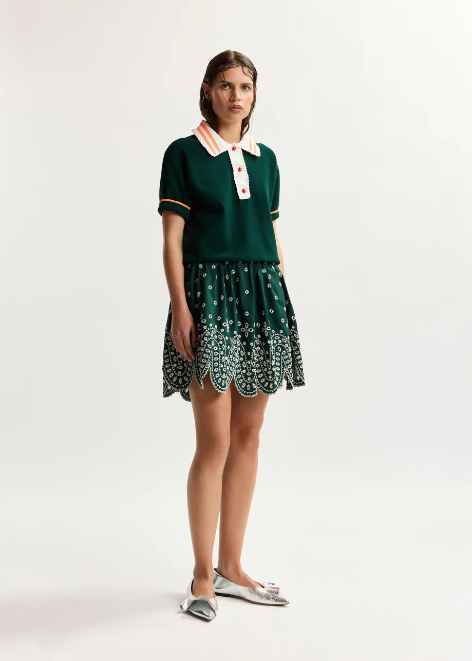 Woman wearing a green dress with a white collar and patterned skirt on a white background
