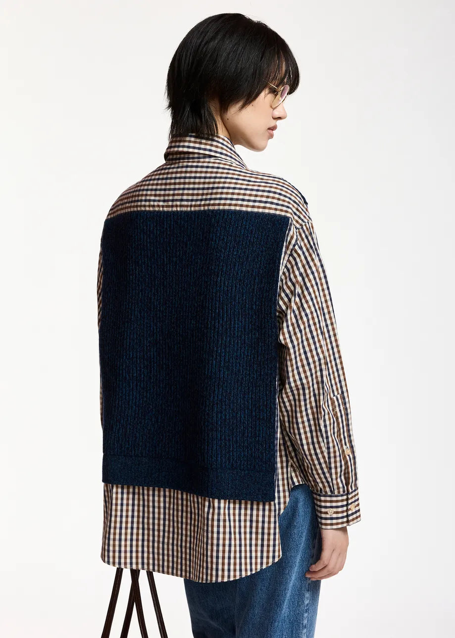 A model with short black hair and glasses wearing a navy blue ribbed knit cardigan over a brown, beige, and white gingham shirt with a matching necktie, against a plain white background.