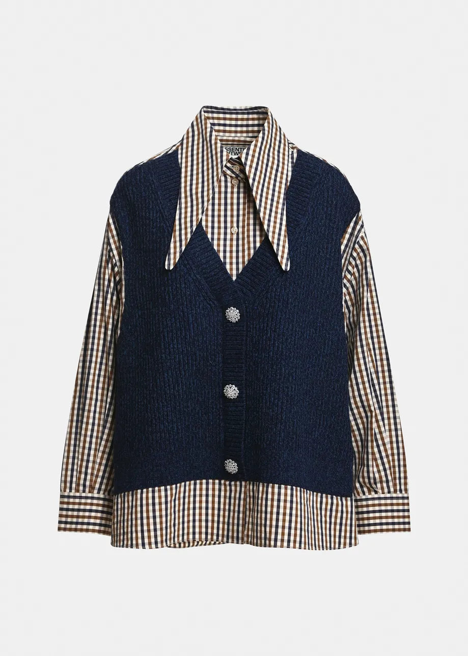 A navy blue knit vest layered over a beige, brown, and white gingham shirt, featuring a pointed collar and three silver buttons on the front, set against a plain light gray background.