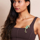 Woman wearing a seahorse brooch on her brown top against a beige background