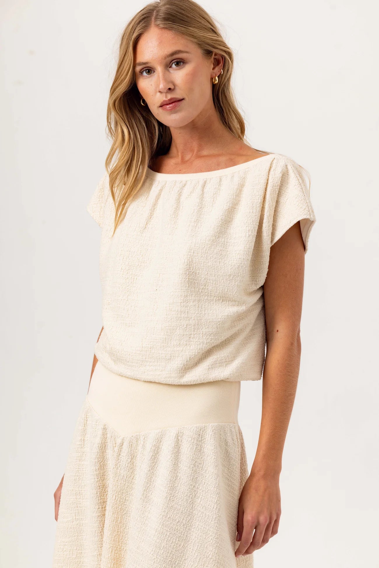 Woman wearing a cream-colored top and skirt set against a plain background