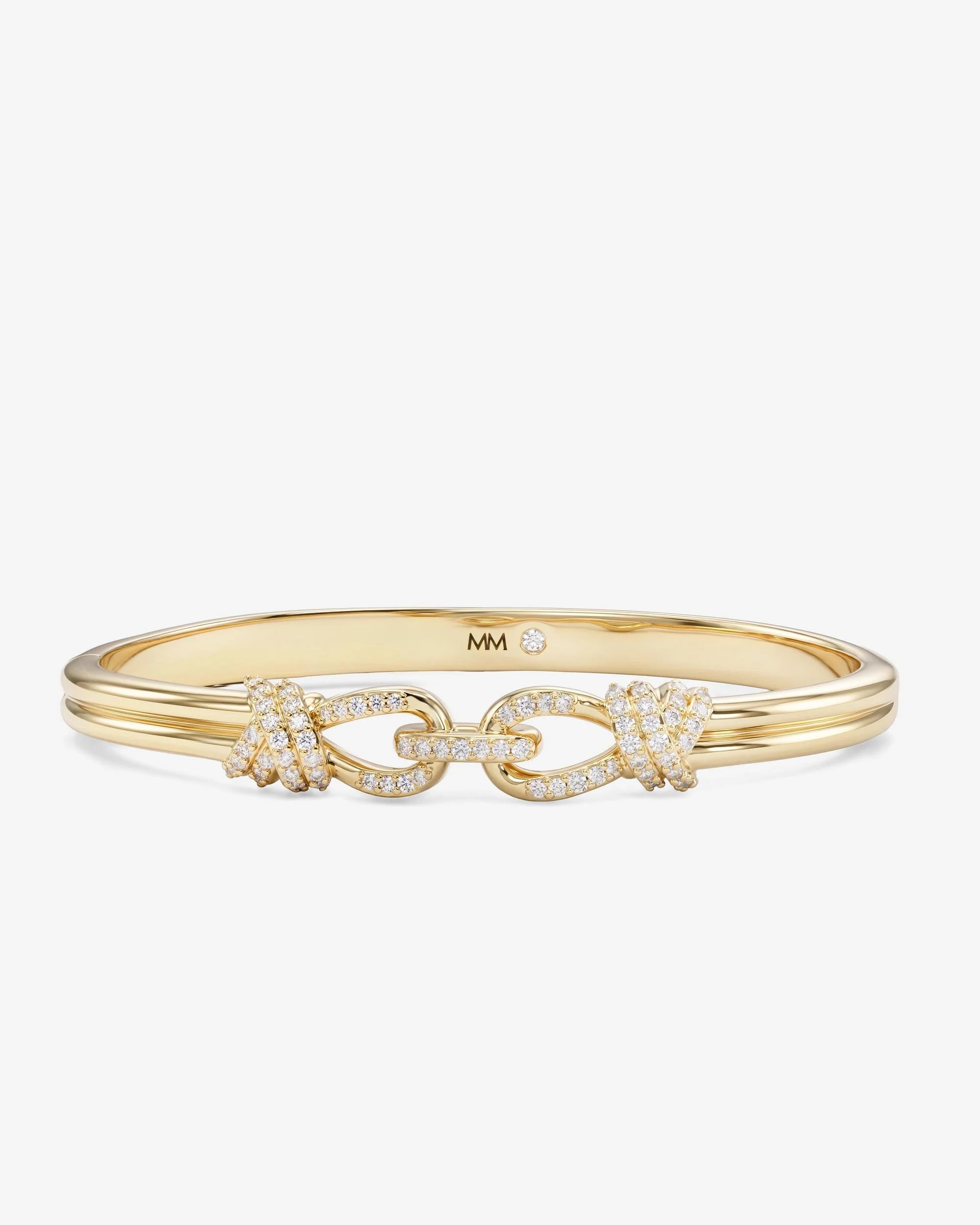 A gold bangle bracelet featuring a central chain-link motif embellished with pavé-set clear stones, shown on a light gray background. The inside of the band is stamped with 'MM'.