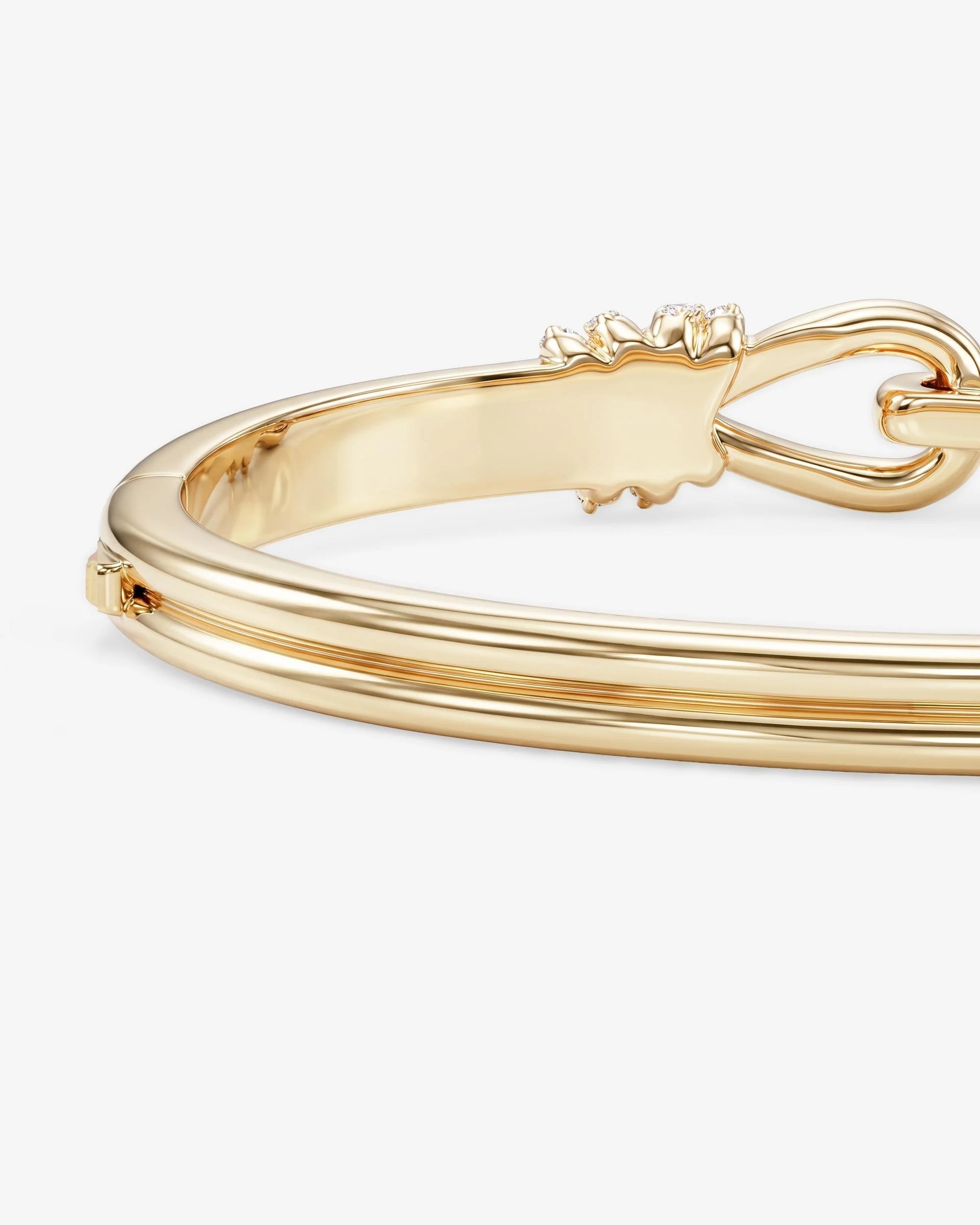 A close-up of a polished gold bangle bracelet showing its double-band design and decorative clasp on a light gray background.