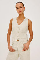 Woman wearing a beige vest and pants against a white background