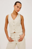 Woman wearing a beige vest and pants against a white background