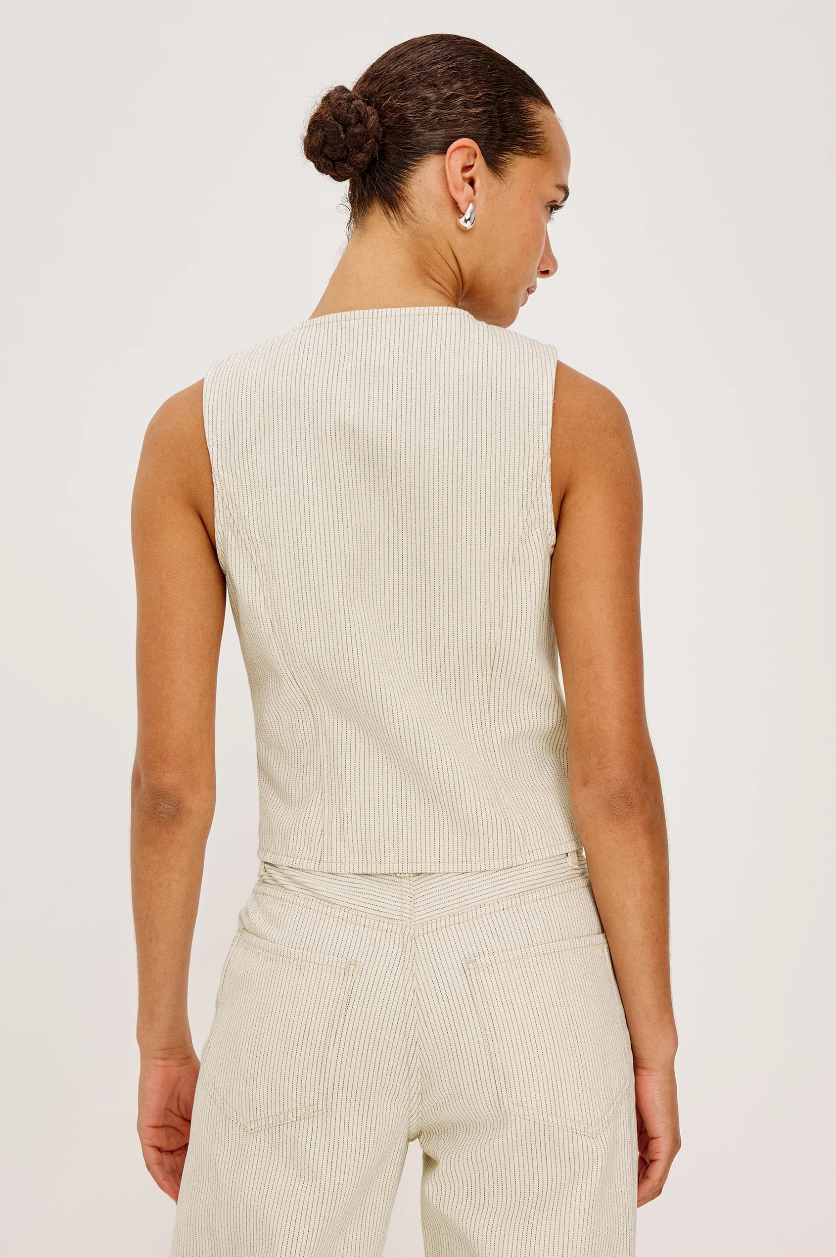 Woman wearing a beige sleeveless top and pants against a white background