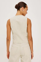 Woman wearing a beige sleeveless top and pants against a white background