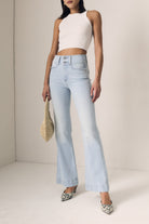Woman wearing light blue jeans and a white top against a plain background