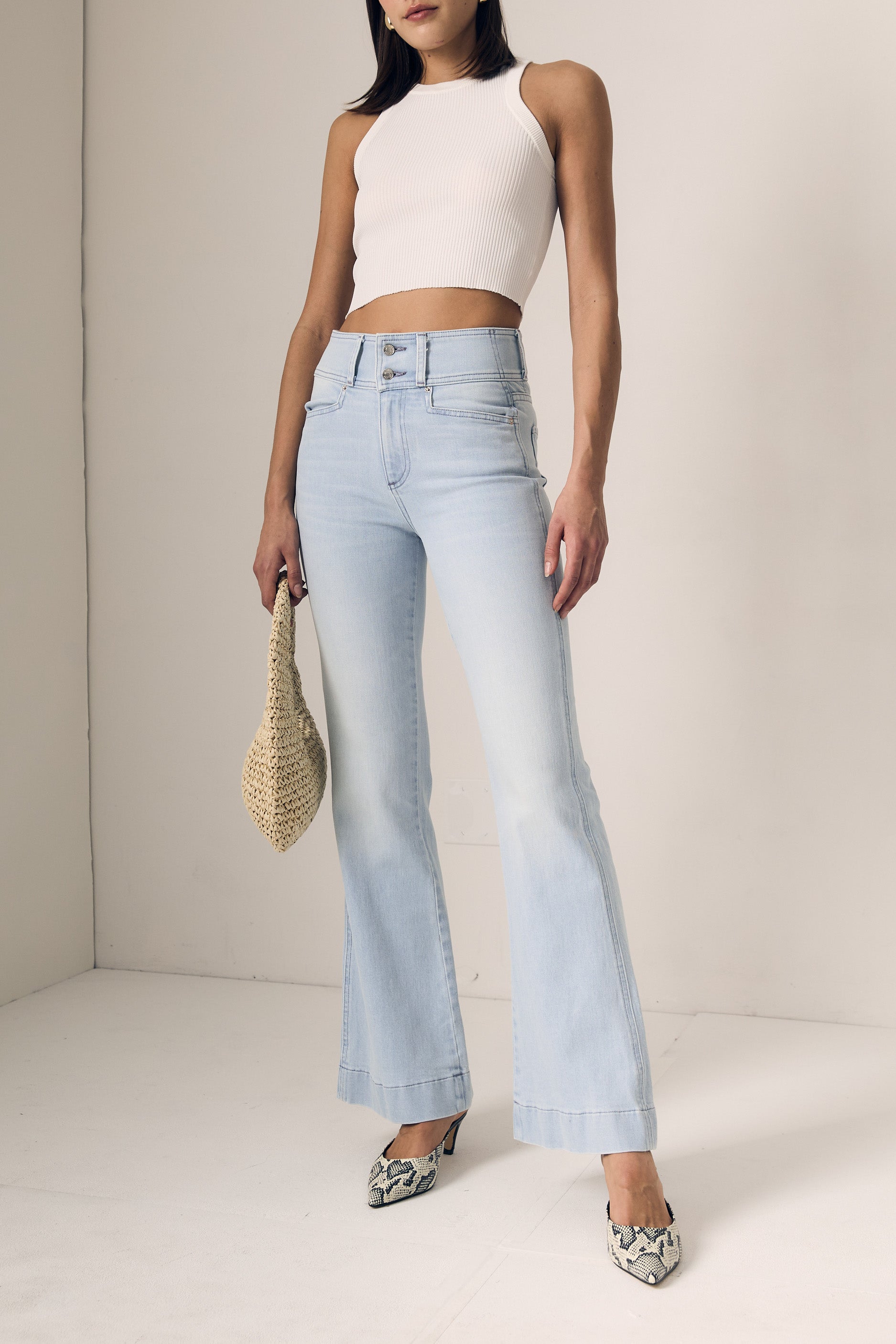 Woman wearing light blue jeans and a white top against a plain background
