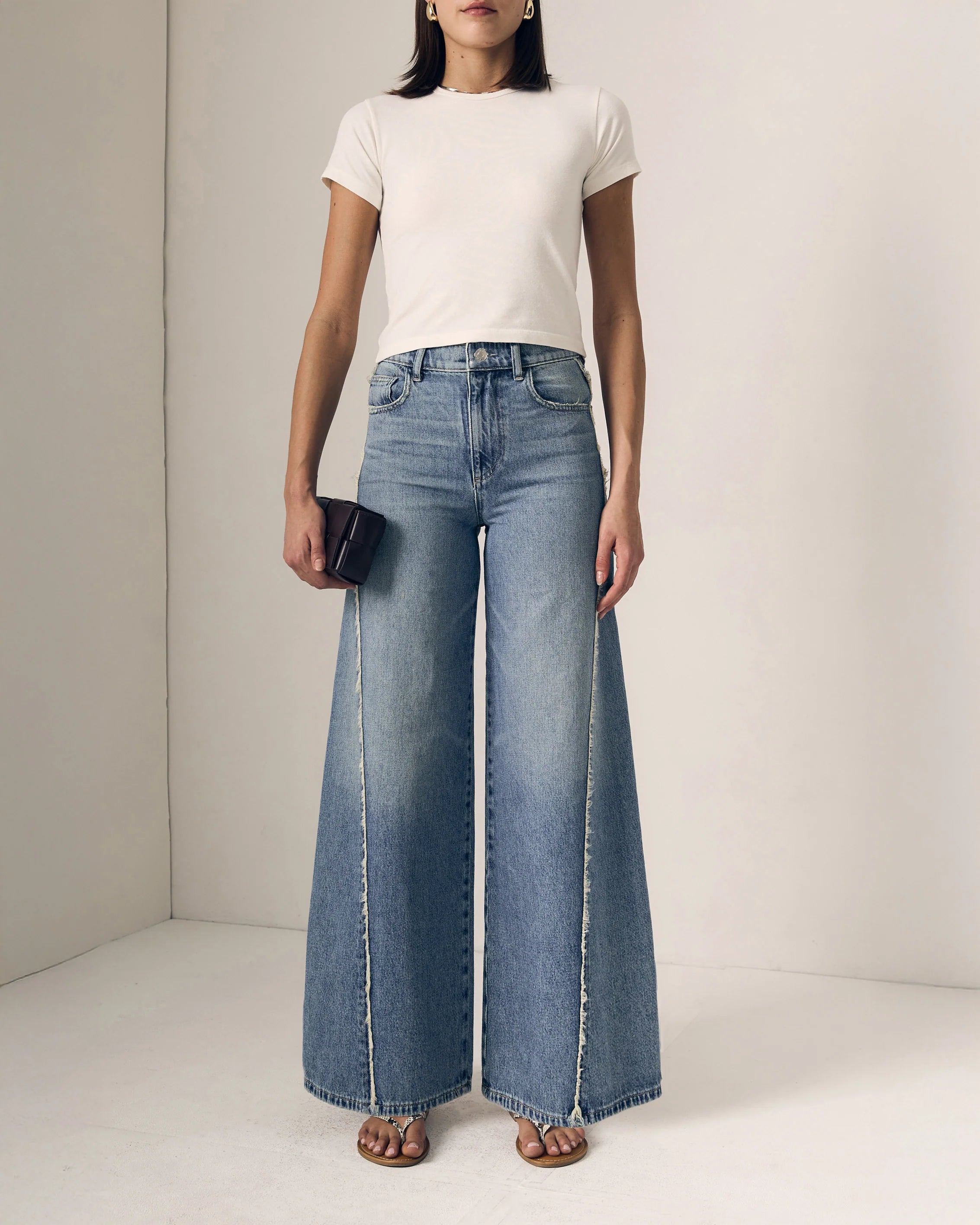 Person wearing a white t-shirt and blue wide-leg jeans against a plain background
