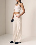 Person wearing a white sleeveless top and cream-colored pants against a plain background