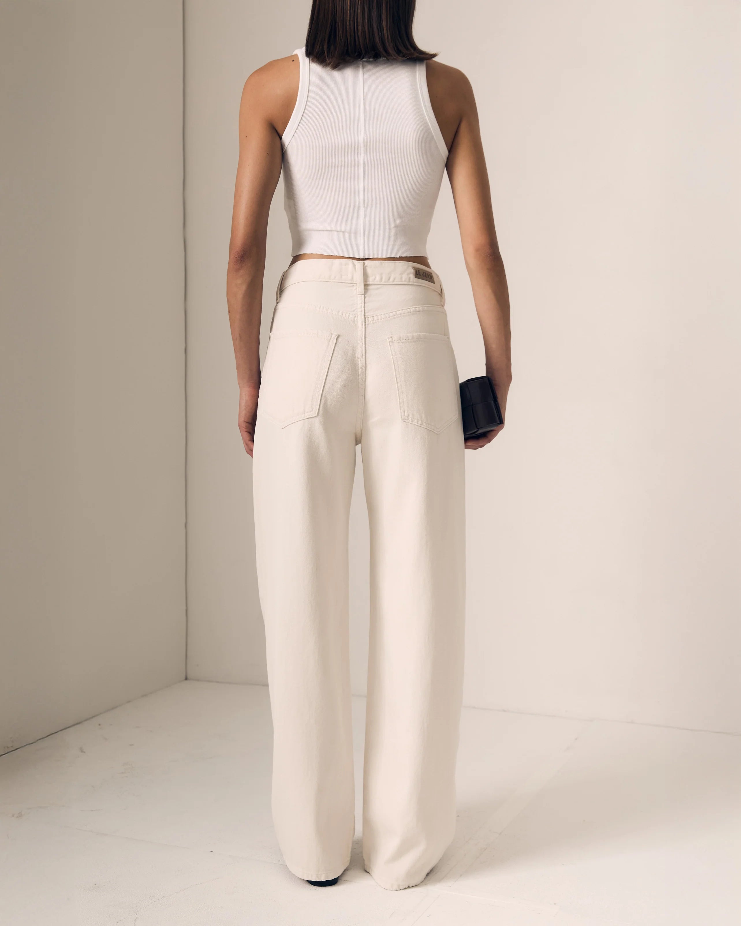 Person wearing a white sleeveless top and beige high-waisted pants against a neutral background