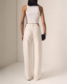 Person wearing a white sleeveless top and beige high-waisted pants against a neutral background