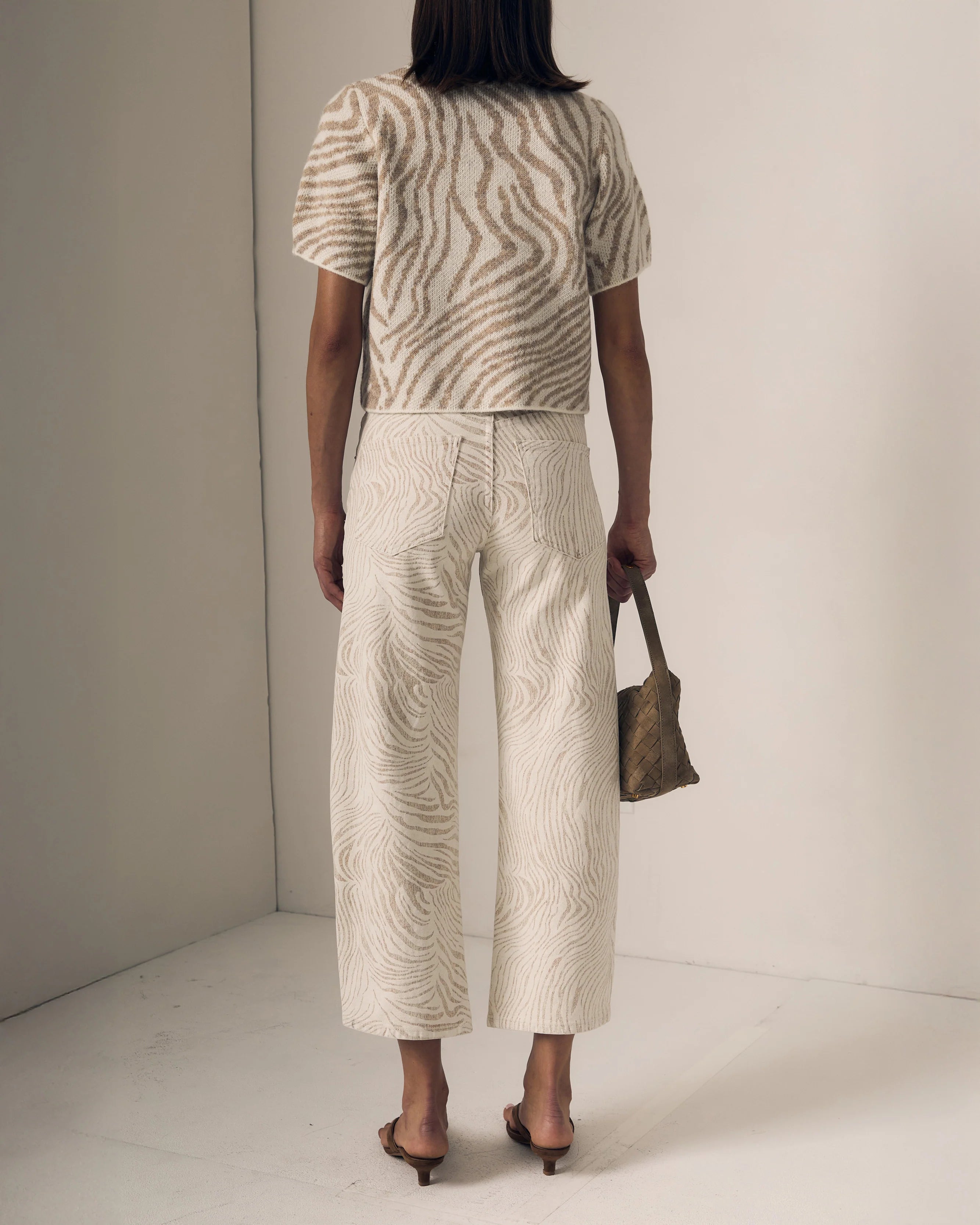 Person wearing a patterned outfit with wide-leg pants and a top, holding a small bag.