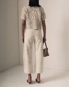 Person wearing a patterned outfit with wide-leg pants and a top, holding a small bag.