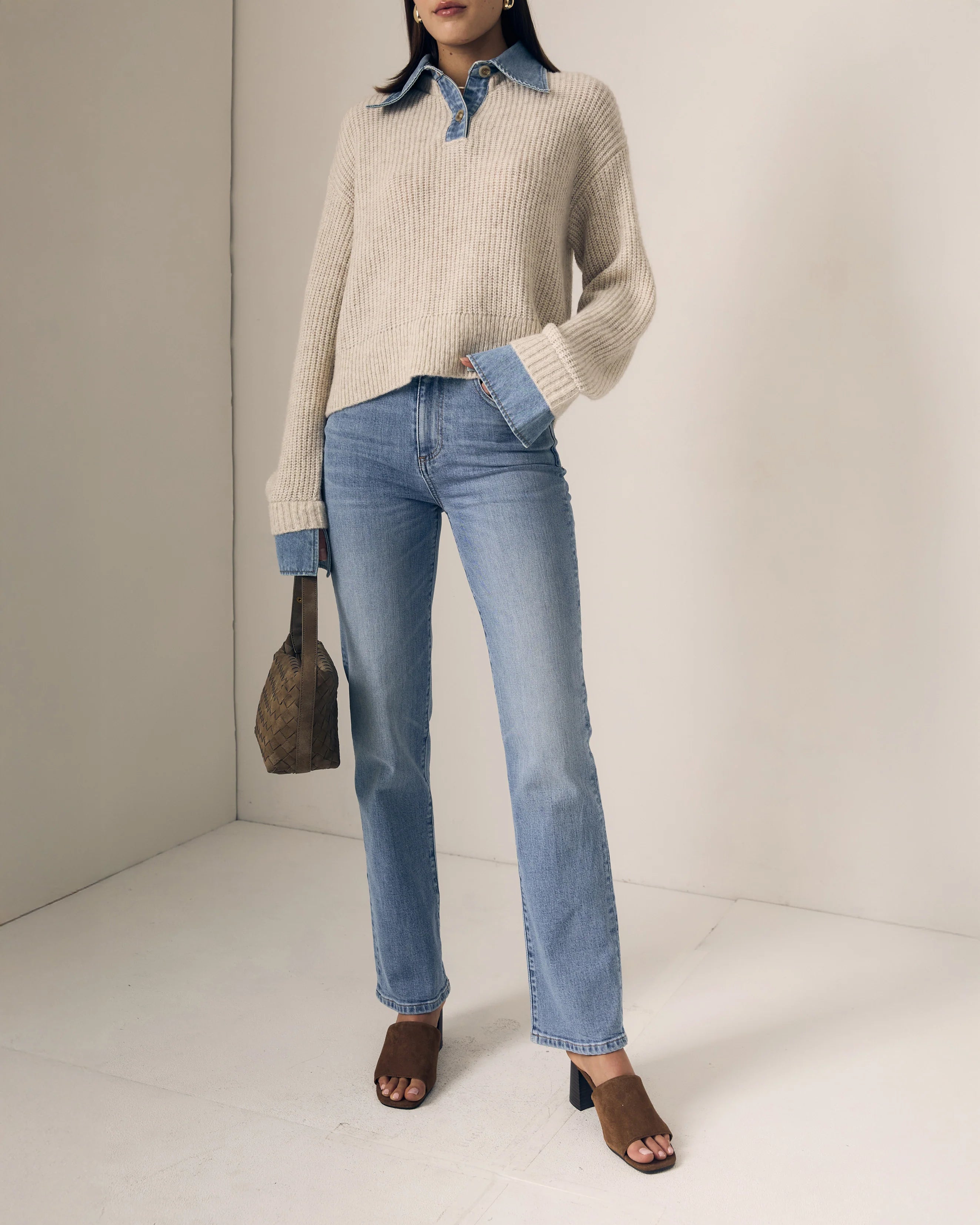 Person wearing a beige sweater, blue jeans, and brown sandals against a neutral background