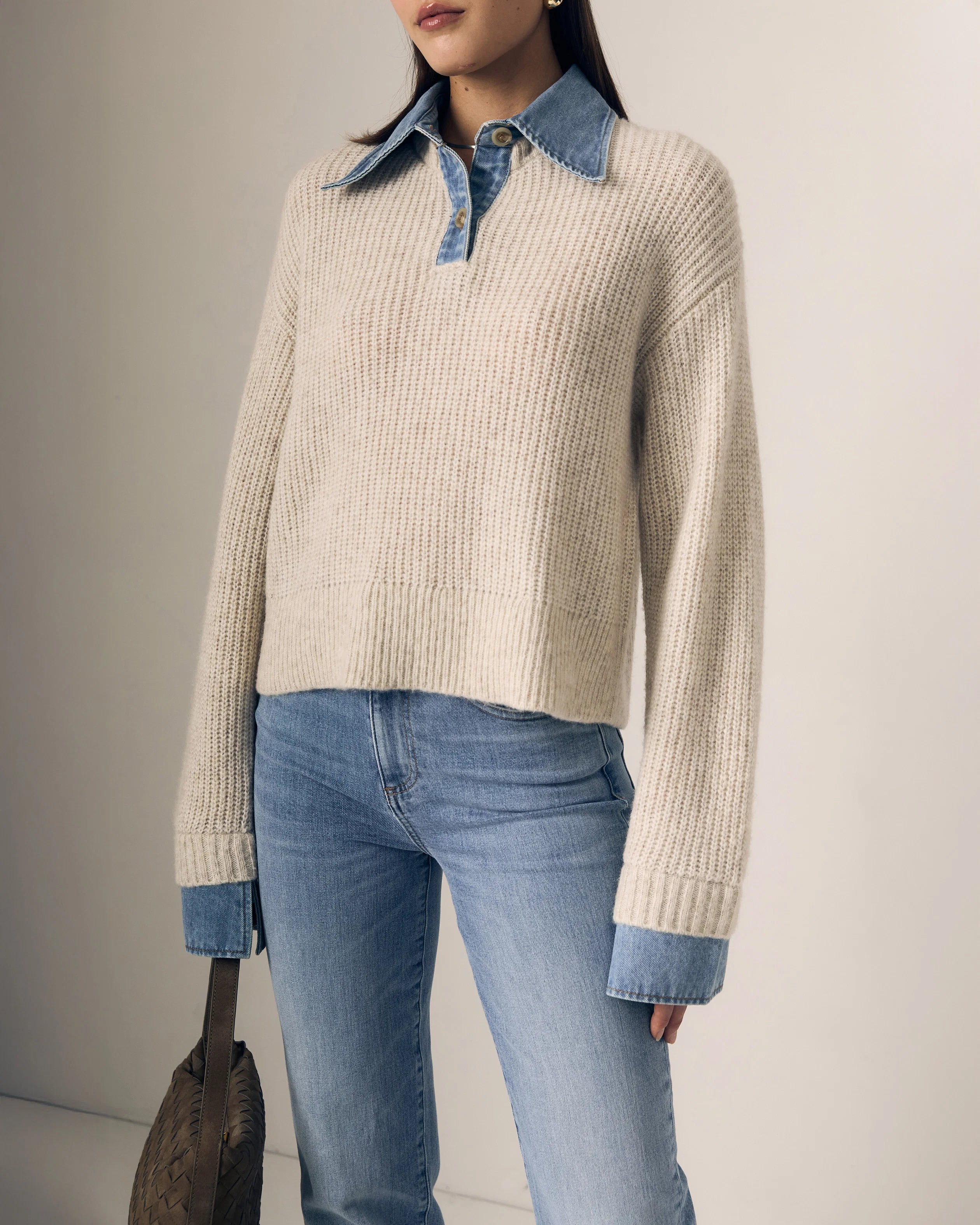 Person wearing a beige sweater with blue collar and cuffs, paired with light blue jeans against a neutral background.