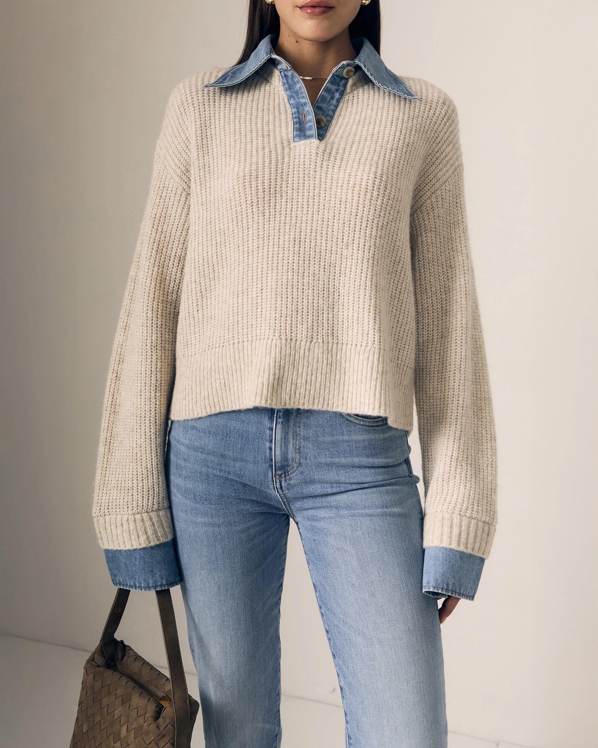 Person wearing a beige sweater with denim collar and cuffs, paired with blue jeans against a neutral background.