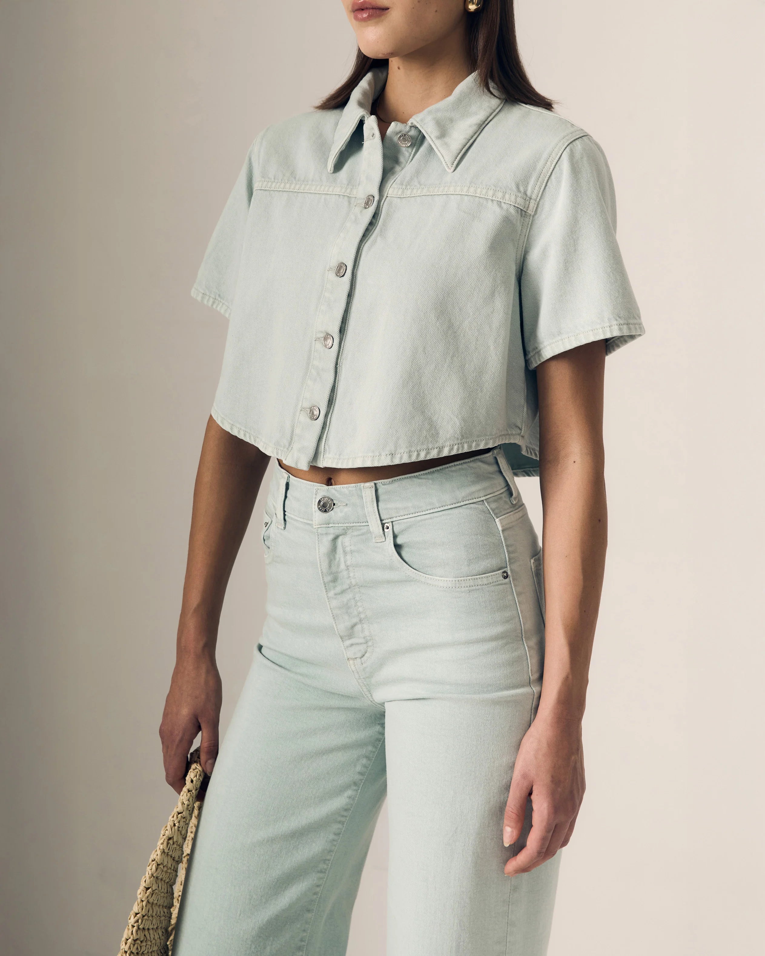 Person wearing a light blue denim shirt and jeans against a neutral background