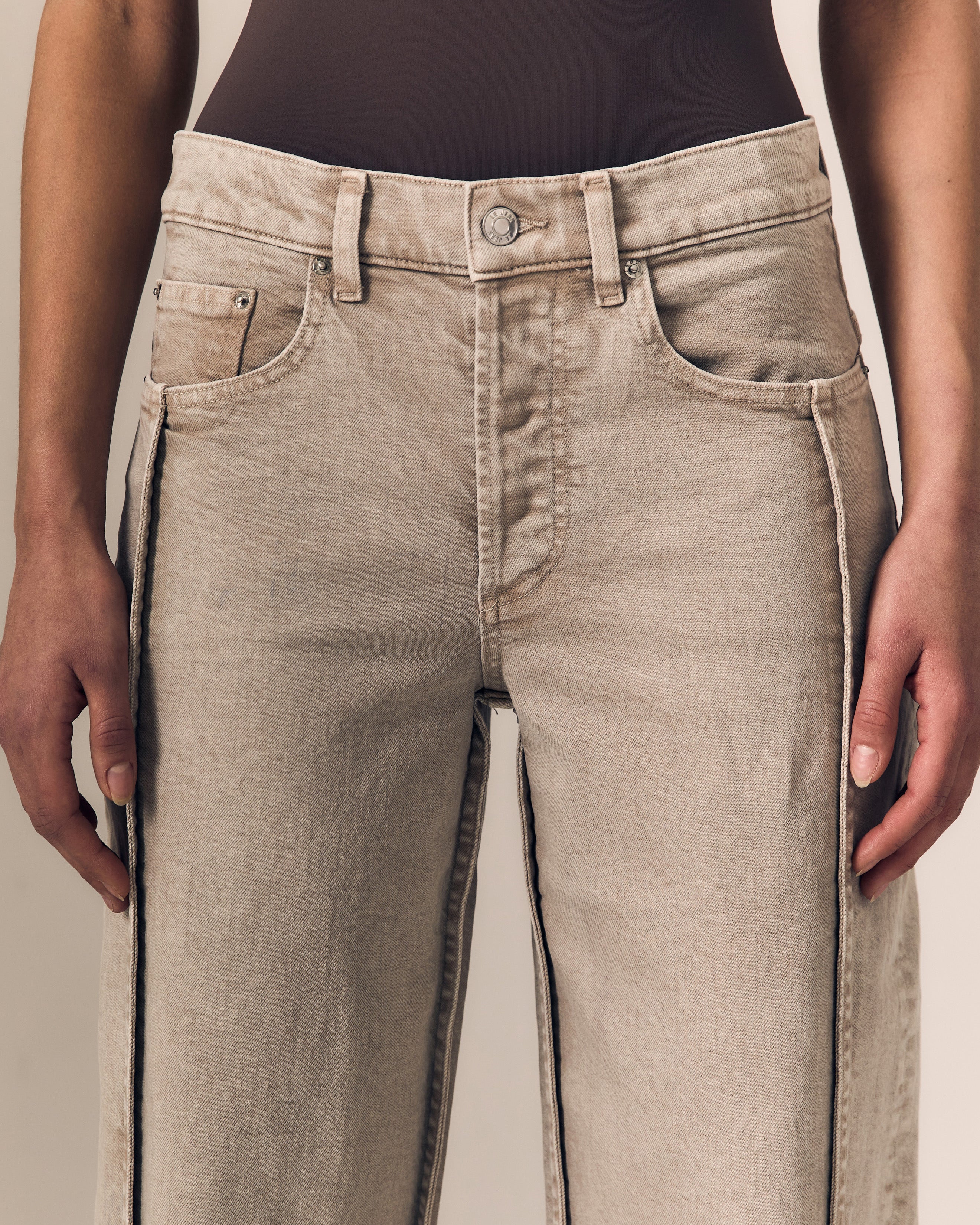 Close-up of a model wearing light beige denim jeans with distinctive dark contrast stitching running down the outer seams of the legs.